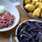 Violette Bohnen, gewürfelter Speck, geschnittene Zwiebeln und frische Kartoffeln als Zutaten für ein Speckbohnen-Gericht.