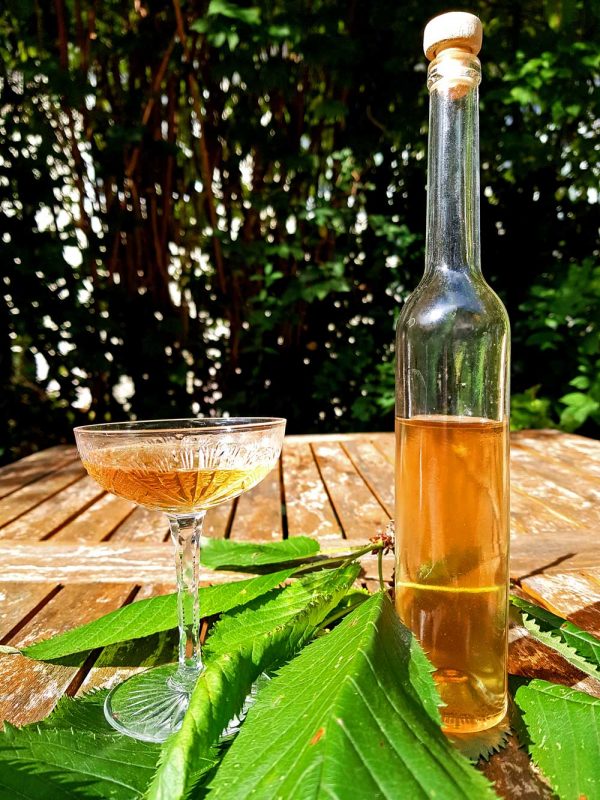 Eine halbleere Flasche steht neben einem vollem Glas auf dem Gartentisch
